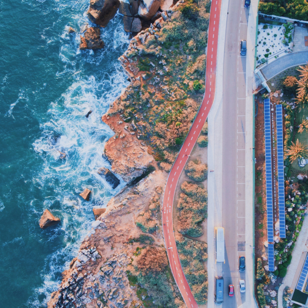 Coastal road in Cascais: Aerial view shows winding cycle path beside ocean, scenic coastal beauty.