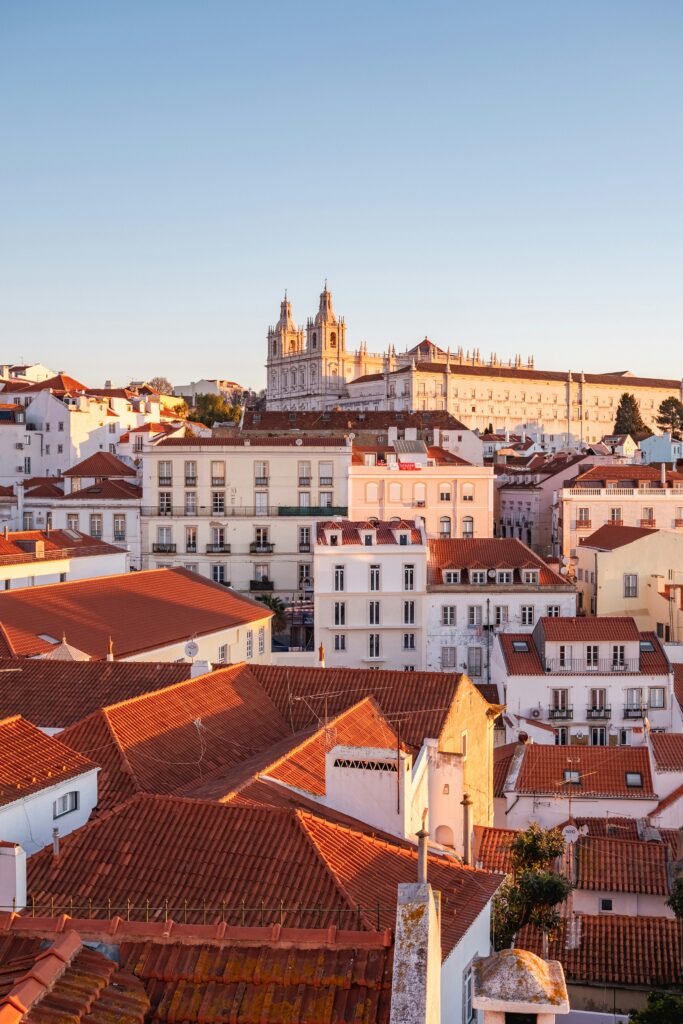 Lisbon aerial view: Red rooftops, Jerónimos Monastery backdrop, bathed in summer evening glow.