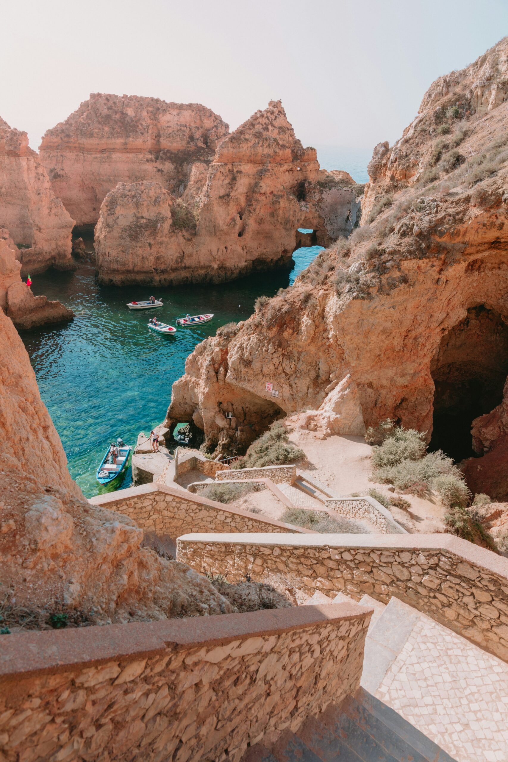 Small boats exploring caves by unique cliffs in the Algarve, set against the backdrop of azure ocean.